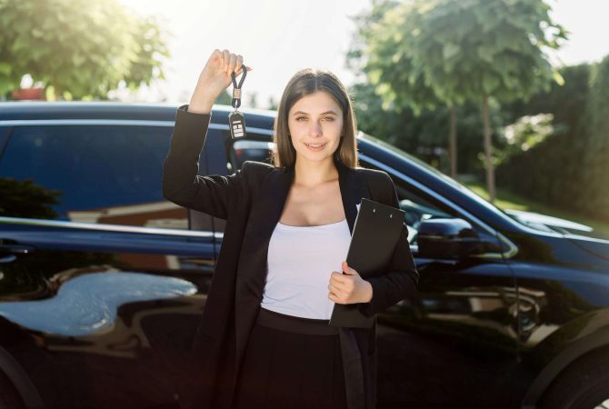 Beautiful girl with car key in hand. Caucasian woman car seller holding car keys, standing in front